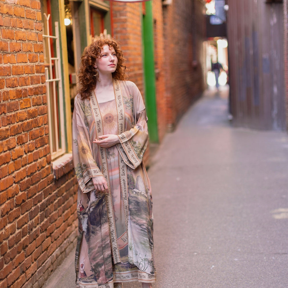
                  
                    Model wearing sun-washed vintage-inspired Opera Duster featuring symbols of friendship, love, and truth in soft lavender, sage, gold, and aqua – Market of Stars
                  
                