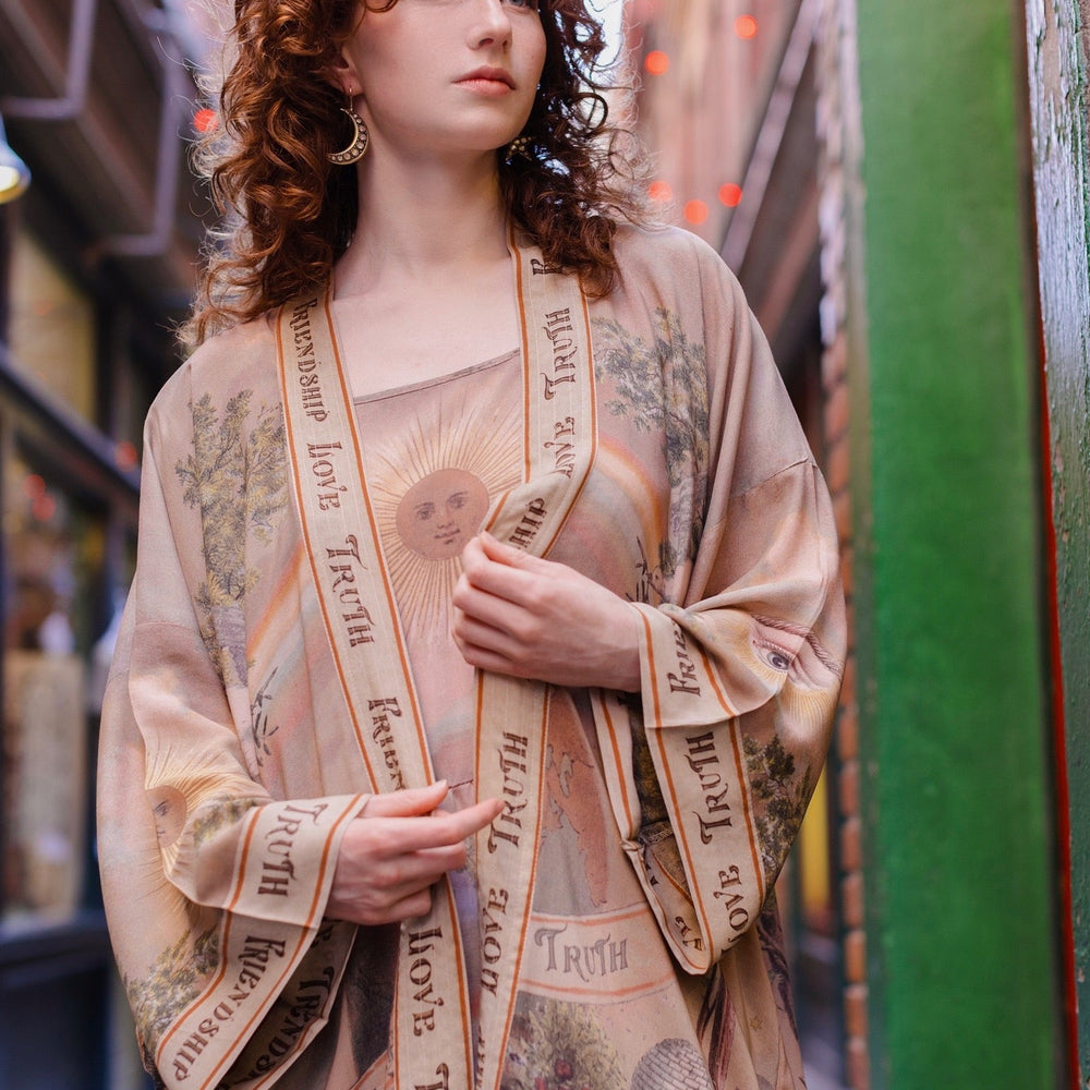 
                  
                    Model wearing sun-washed vintage-inspired Opera Duster featuring symbols of friendship, love, and truth in soft lavender, sage, gold, and aqua – Market of Stars
                  
                