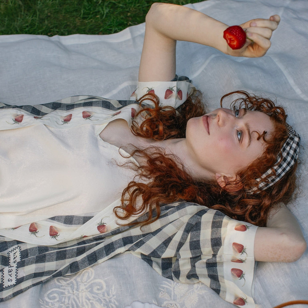 
                  
                    Model wearing Happy Days pixie cut kimono featuring heritage gingham, vintage strawberries, and a cross-stitch patch inspired by an 1836 sampler – Market of Stars.
                  
                