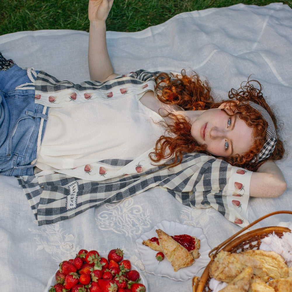 
                  
                    Model wearing Happy Days pixie cut kimono featuring heritage gingham, vintage strawberries, and a cross-stitch patch inspired by an 1836 sampler – Market of Stars.
                  
                