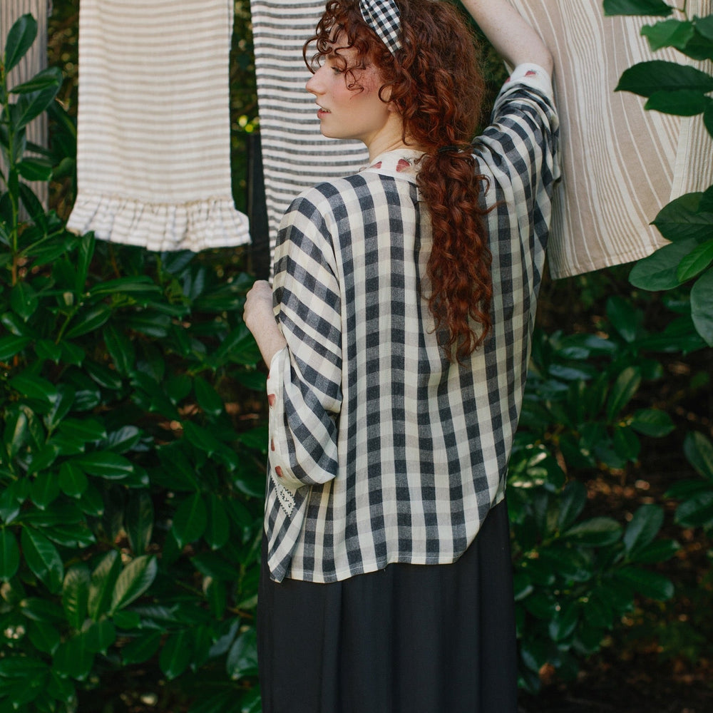 
                  
                    Model wearing Happy Days pixie cut kimono featuring heritage gingham, vintage strawberries, and a cross-stitch patch inspired by an 1836 sampler – Market of Stars.
                  
                