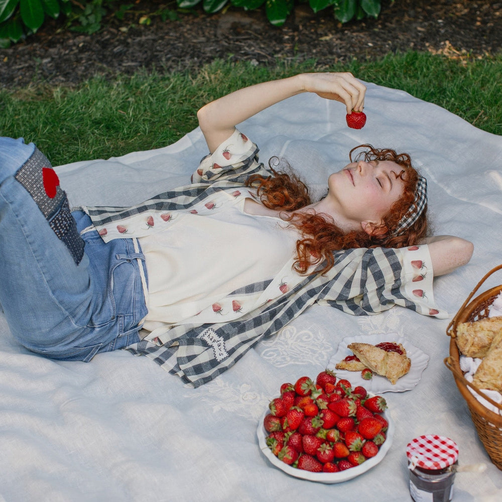 
                  
                    Model wearing Happy Days pixie cut kimono featuring heritage gingham, vintage strawberries, and a cross-stitch patch inspired by an 1836 sampler – Market of Stars.
                  
                