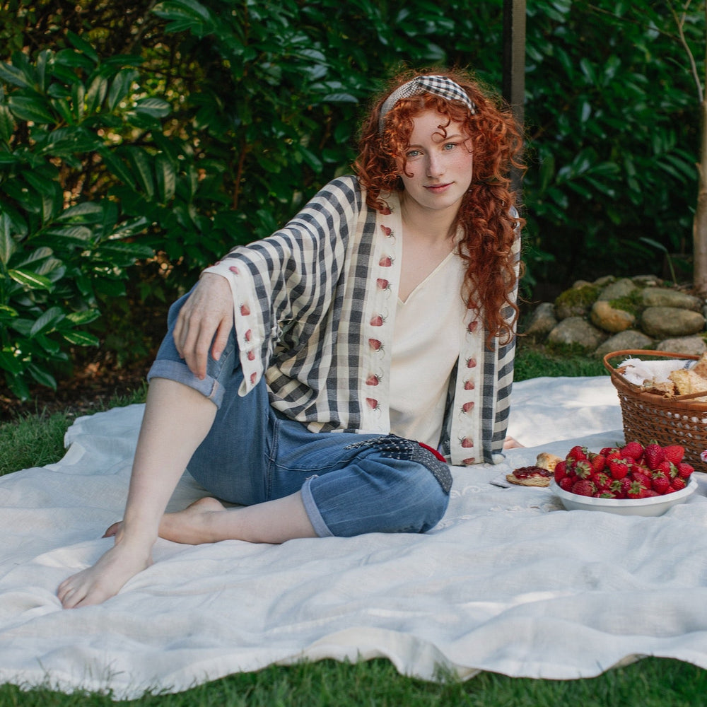 
                  
                    Model wearing Happy Days pixie cut kimono featuring heritage gingham, vintage strawberries, and a cross-stitch patch inspired by an 1836 sampler – Market of Stars.
                  
                