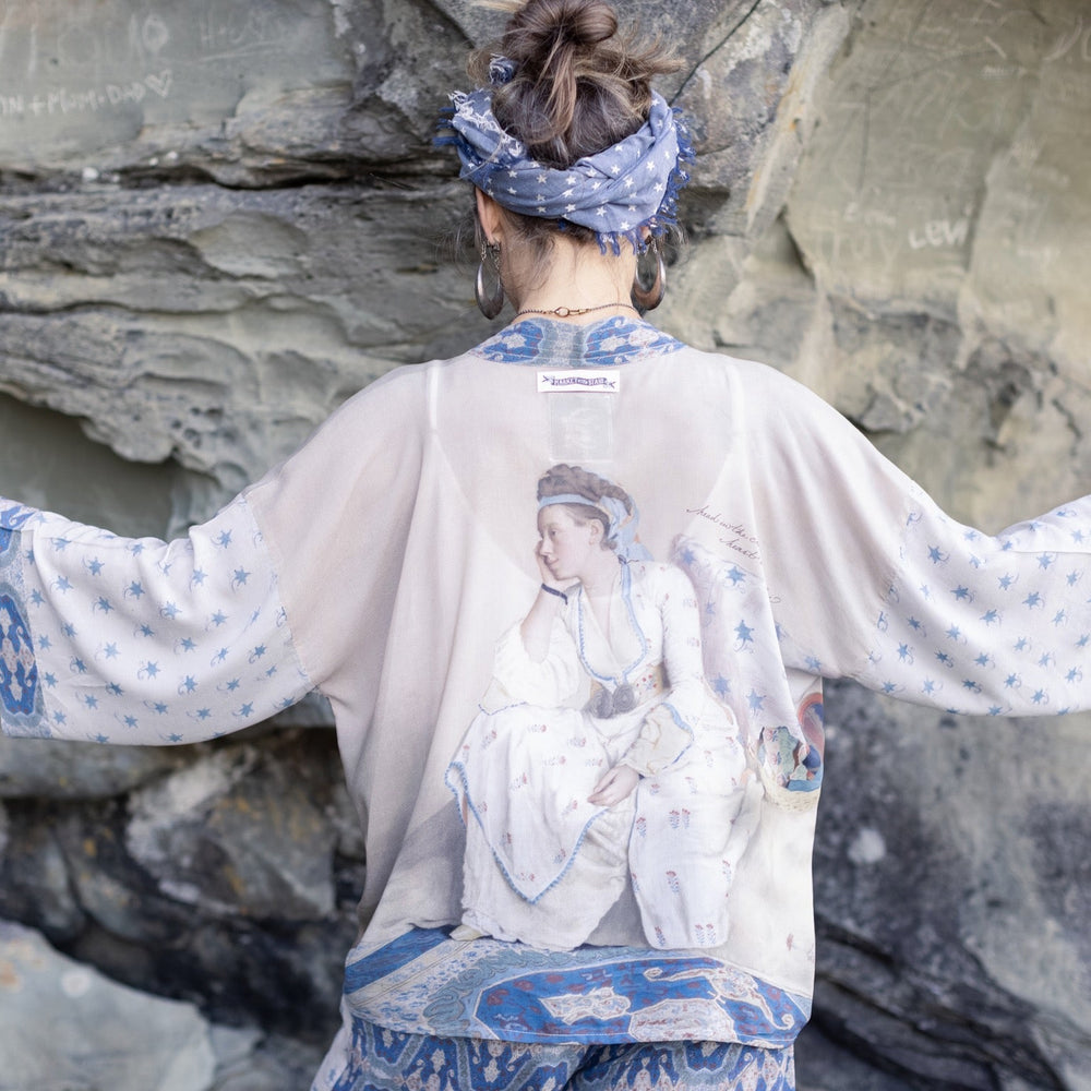 
                  
                    Model wearing the Head in the Clouds Opera Duster featuring Liotard’s portrait of his wife with Turkish textiles, starry sleeves, and poetic script – Market of Stars.
                  
                
