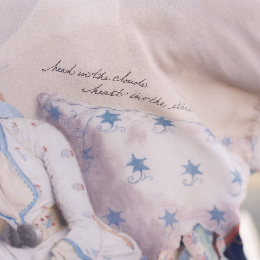 
                  
                    Model wearing the Head in the Clouds Opera Duster featuring Liotard’s portrait of his wife with Turkish textiles, starry sleeves, and poetic script – Market of Stars.
                  
                