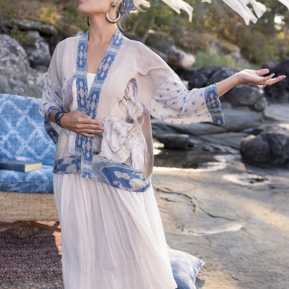 
                  
                    Model wearing the Head in the Clouds Opera Duster featuring Liotard’s portrait of his wife with Turkish textiles, starry sleeves, and poetic script – Market of Stars.
                  
                