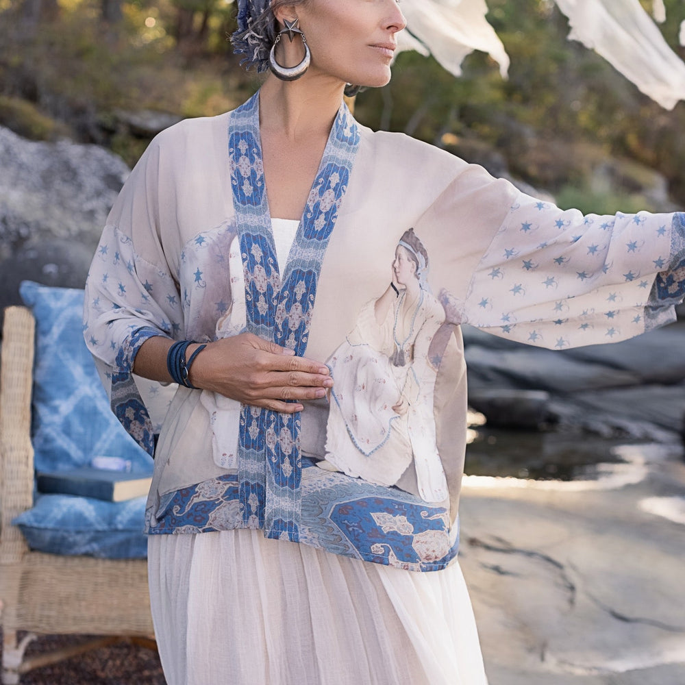 
                  
                    Model wearing the Head in the Clouds Opera Duster featuring Liotard’s portrait of his wife with Turkish textiles, starry sleeves, and poetic script – Market of Stars.
                  
                