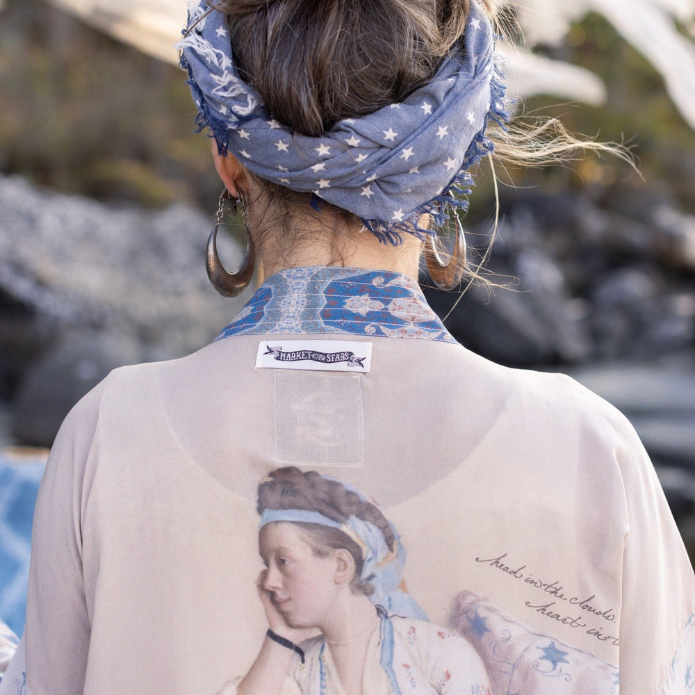 
                  
                    Model wearing the Head in the Clouds Opera Duster featuring Liotard’s portrait of his wife with Turkish textiles, starry sleeves, and poetic script – Market of Stars.
                  
                