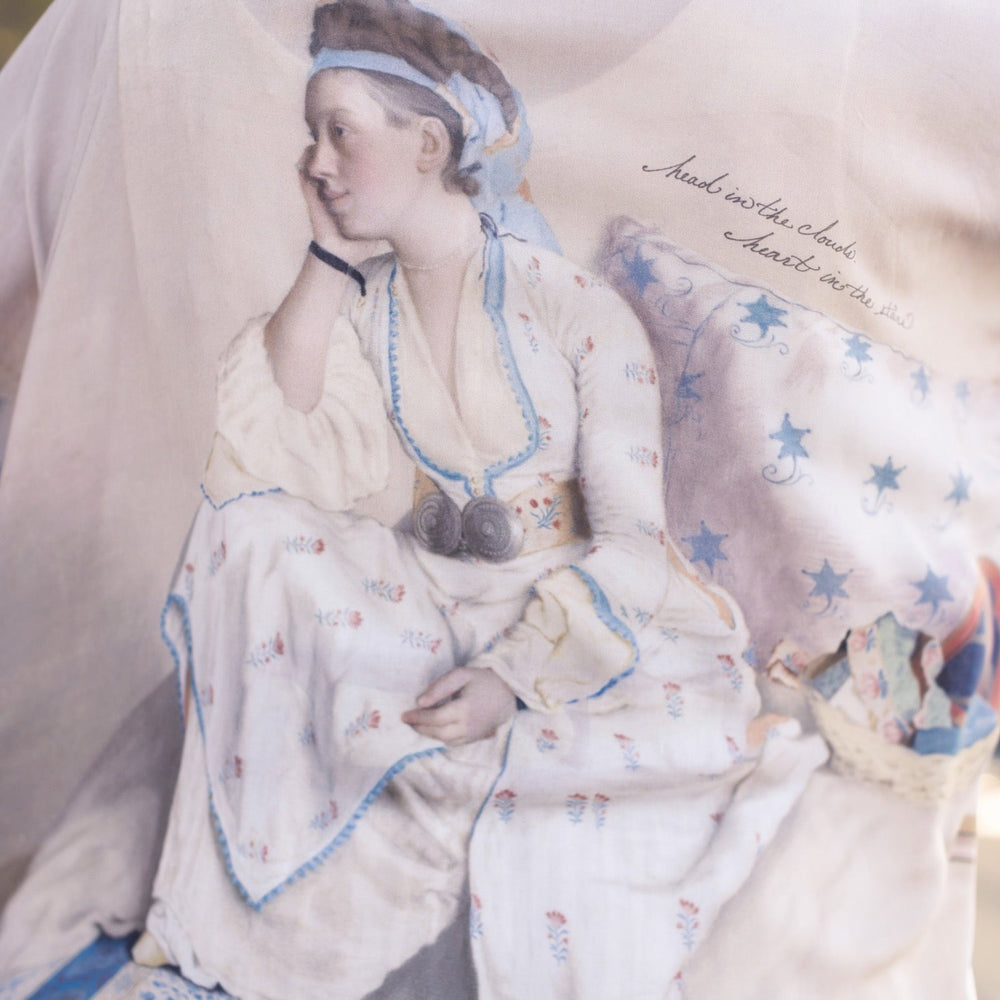 
                  
                    Model wearing the Head in the Clouds Opera Duster featuring Liotard’s portrait of his wife with Turkish textiles, starry sleeves, and poetic script – Market of Stars.
                  
                