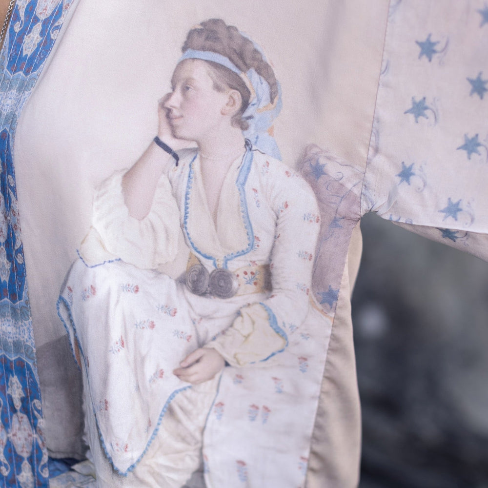 
                  
                    Model wearing the Head in the Clouds Opera Duster featuring Liotard’s portrait of his wife with Turkish textiles, starry sleeves, and poetic script – Market of Stars.
                  
                