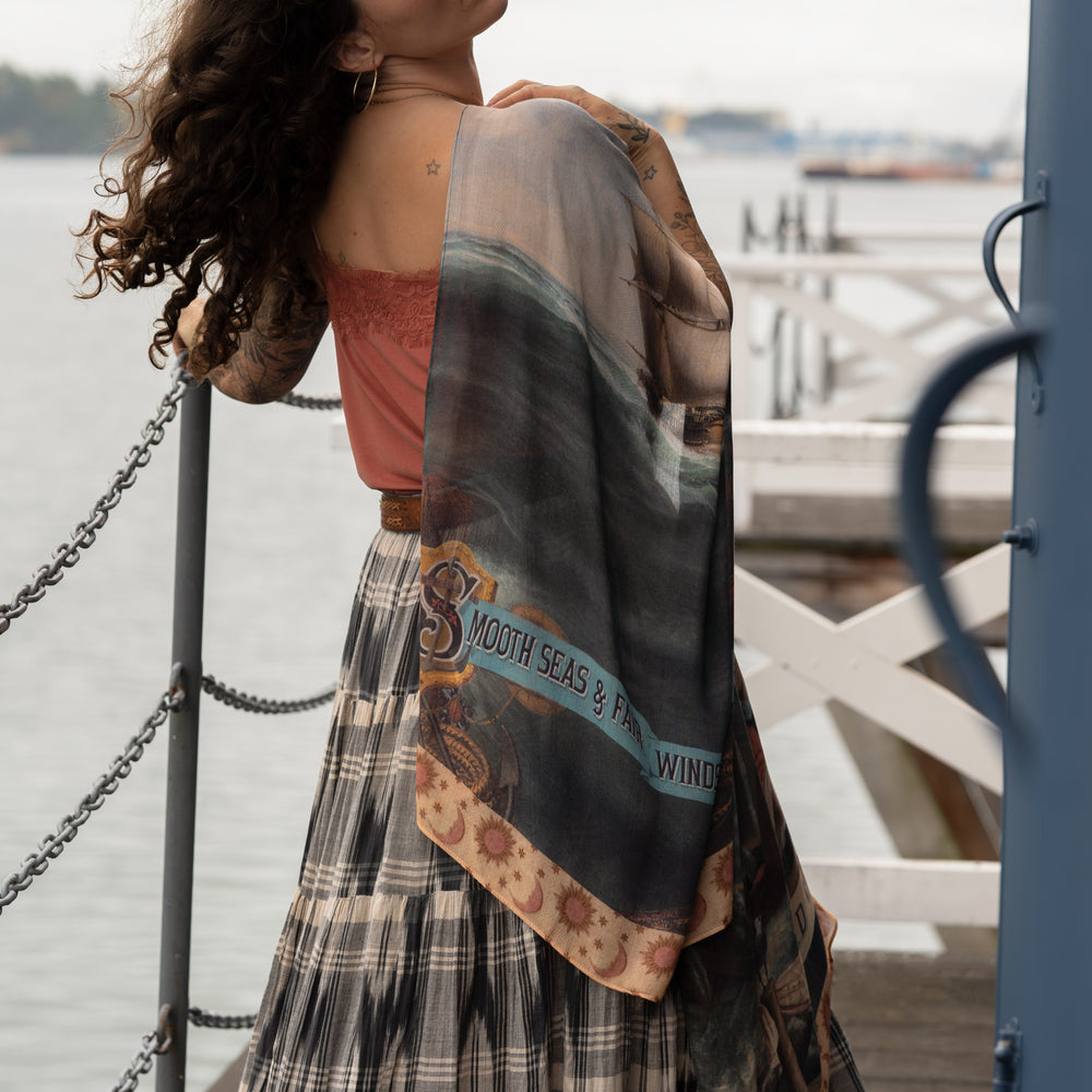 Model wearing the Hold Fast bamboo viscose scarf featuring a Victorian woman bravely rowing through a storm, seagulls, and rainbow horizon – Market of Stars.