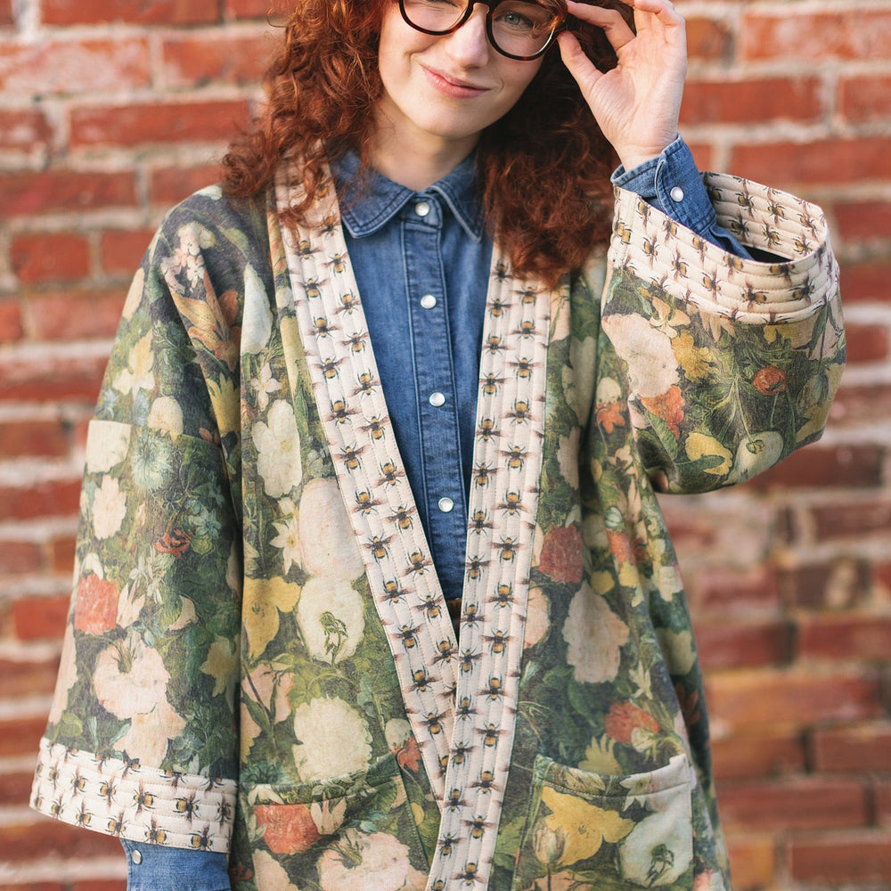 
                  
                    Model wearing the I Dream in Flowers Cottage Cardigan featuring painterly floral artwork and Victorian bumblebee trim, perfect for cozy layering – Market of Stars
                  
                