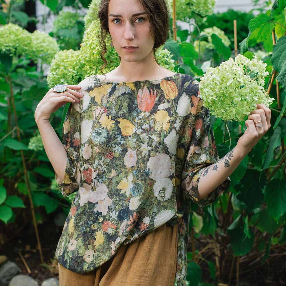 
                  
                    Model wearing the I Dream in Flowers Luxe Tee featuring painterly florals by Jan Brueghel and hidden bumblebee trim – Market of Stars.
                  
                