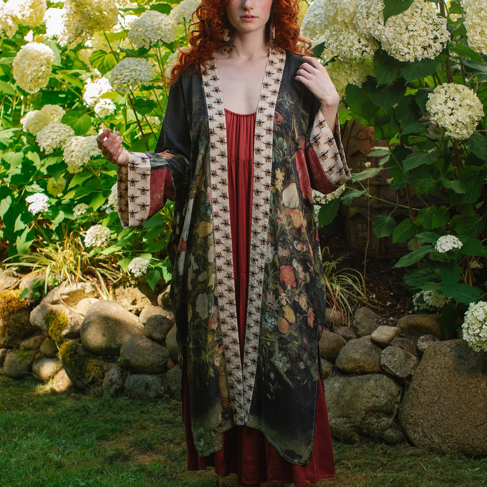 
                  
                    Model wearing the I Dream in Flowers Opera Duster featuring floral oil painting by Jan Brueghel and Victorian bumblebee trim – Market of Stars.
                  
                
