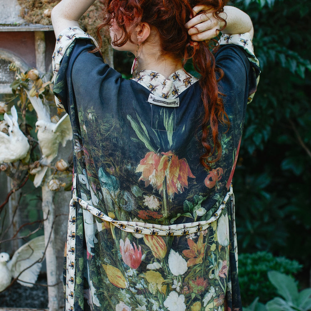 
                  
                    Model wearing the I Dream in Flowers Opera Duster featuring floral oil painting by Jan Brueghel and Victorian bumblebee trim – Market of Stars.
                  
                