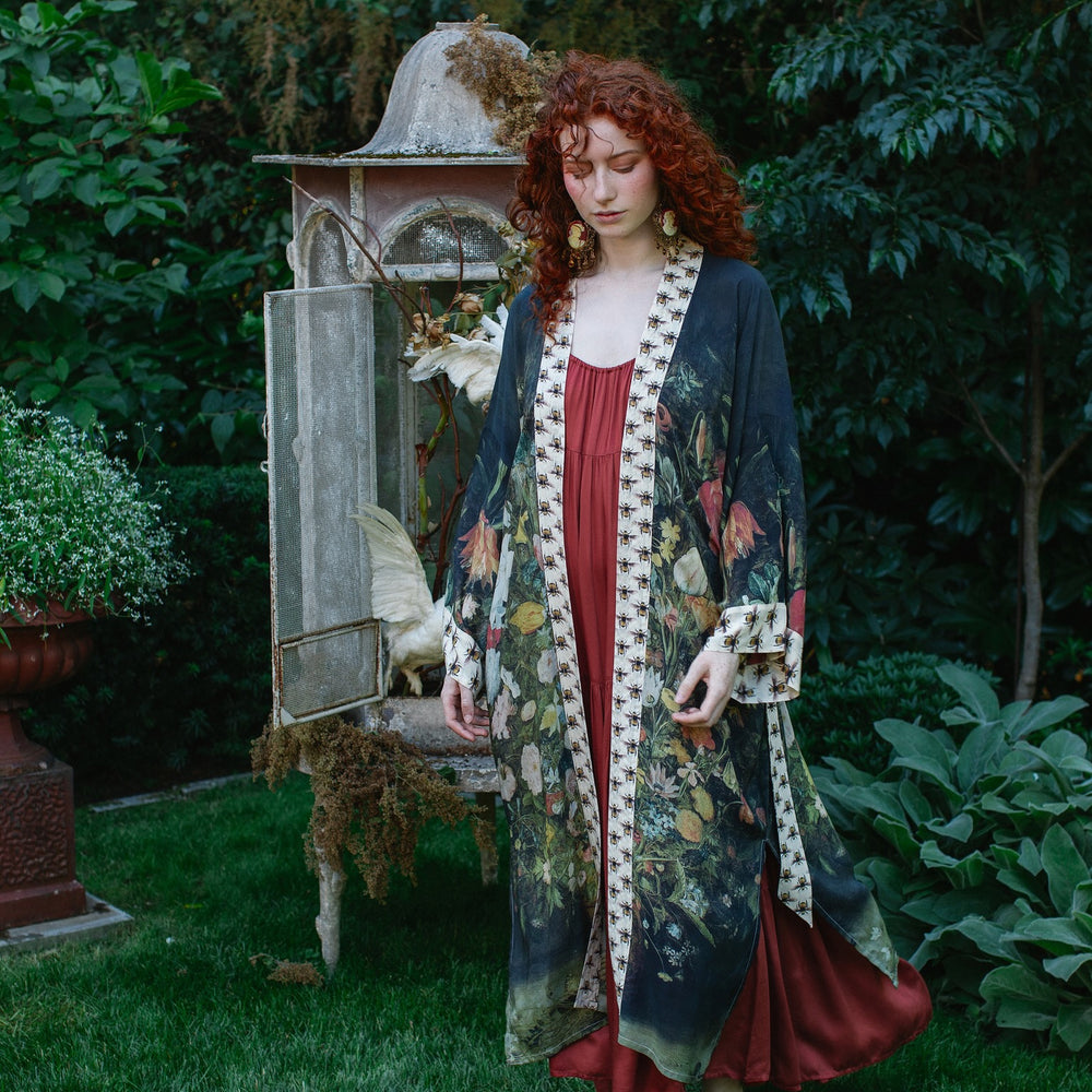 
                  
                    Model wearing the I Dream in Flowers Opera Duster featuring floral oil painting by Jan Brueghel and Victorian bumblebee trim – Market of Stars.
                  
                