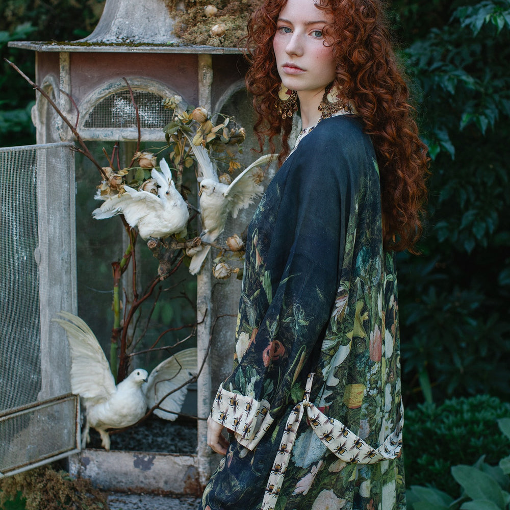 
                  
                    Model wearing the I Dream in Flowers Opera Duster featuring floral oil painting by Jan Brueghel and Victorian bumblebee trim – Market of Stars.
                  
                