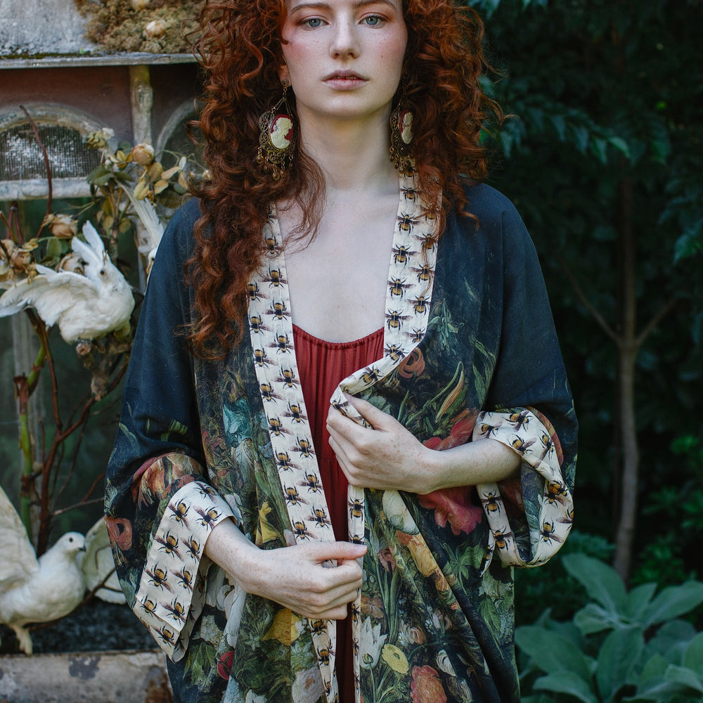 
                  
                    Model wearing the I Dream in Flowers Opera Duster featuring floral oil painting by Jan Brueghel and Victorian bumblebee trim – Market of Stars.
                  
                