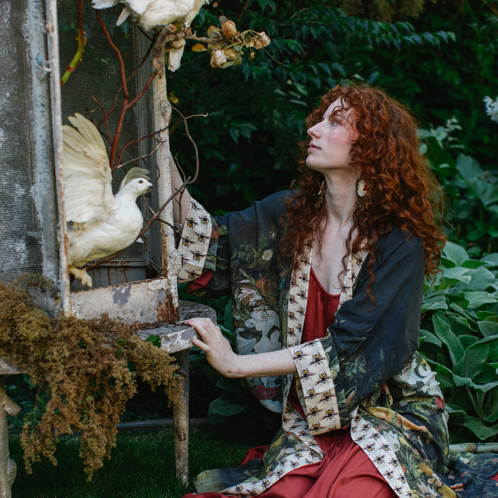 
                  
                    Model wearing the I Dream in Flowers Opera Duster featuring floral oil painting by Jan Brueghel and Victorian bumblebee trim – Market of Stars.
                  
                