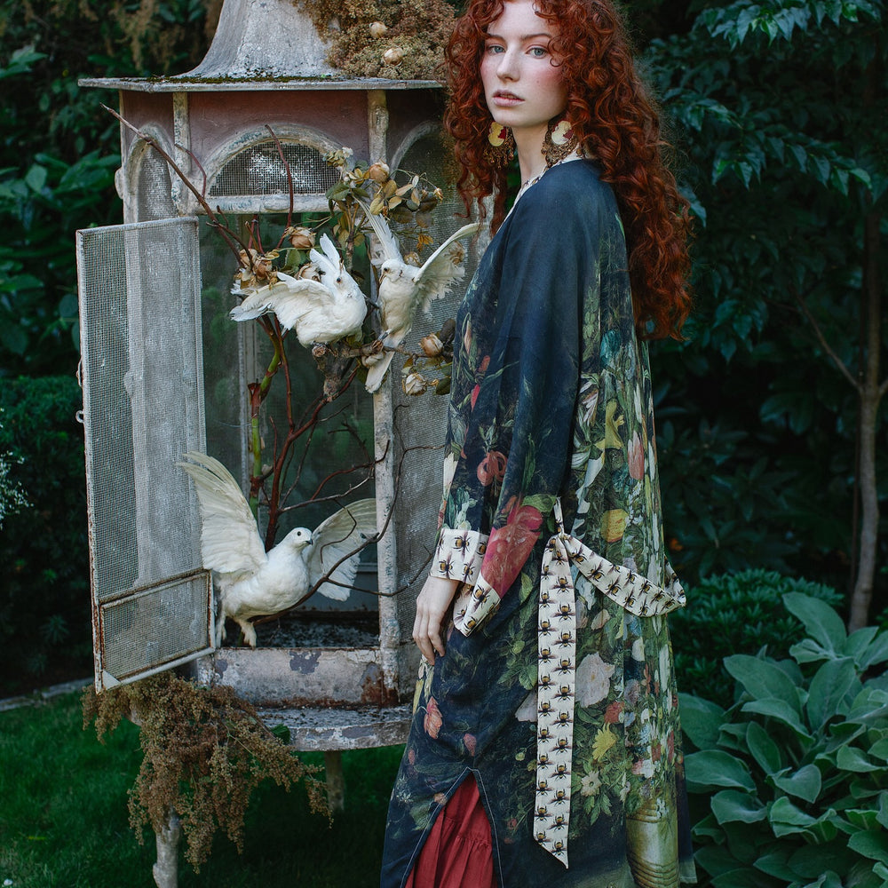 
                  
                    Model wearing the I Dream in Flowers Opera Duster featuring floral oil painting by Jan Brueghel and Victorian bumblebee trim – Market of Stars.
                  
                