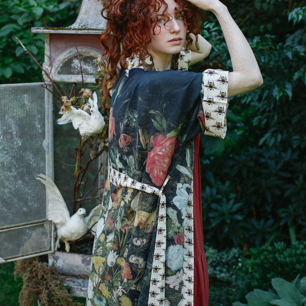 
                  
                    Model wearing the I Dream in Flowers Opera Duster featuring floral oil painting by Jan Brueghel and Victorian bumblebee trim – Market of Stars.
                  
                