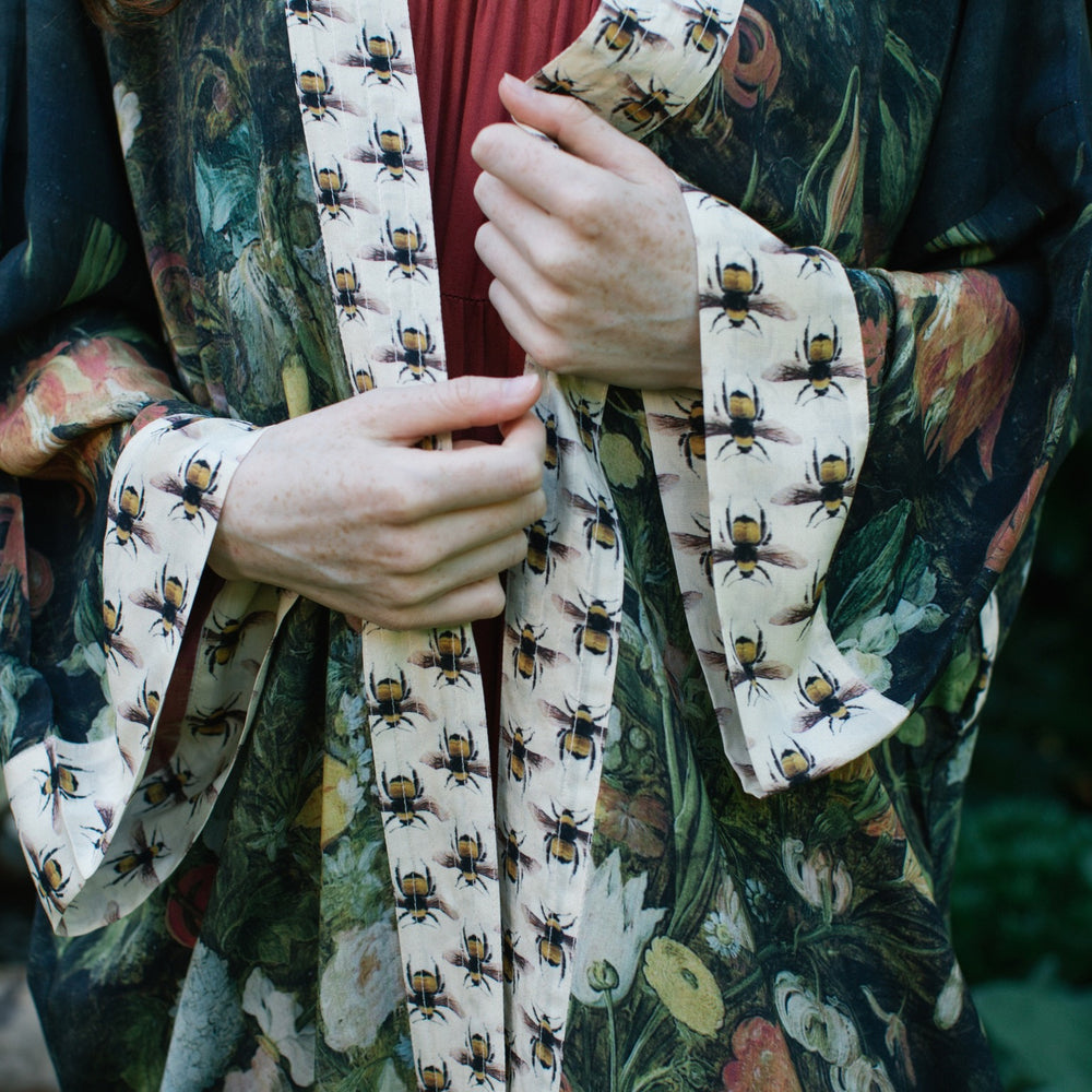 
                  
                    Model wearing the I Dream in Flowers Opera Duster featuring floral oil painting by Jan Brueghel and Victorian bumblebee trim – Market of Stars.
                  
                