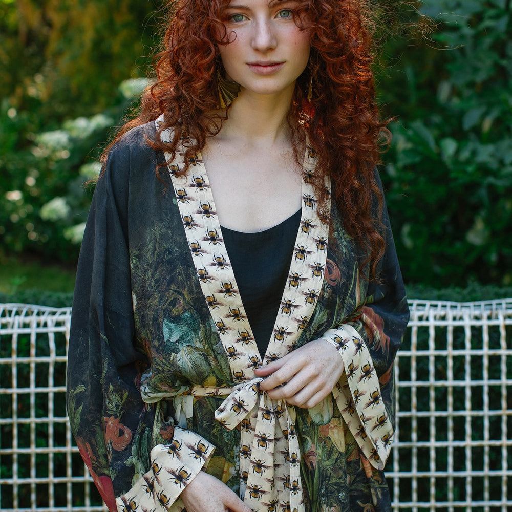 
                  
                    Model wearing the I Dream in Flowers Opera Duster featuring floral oil painting by Jan Brueghel and Victorian bumblebee trim – Market of Stars.
                  
                