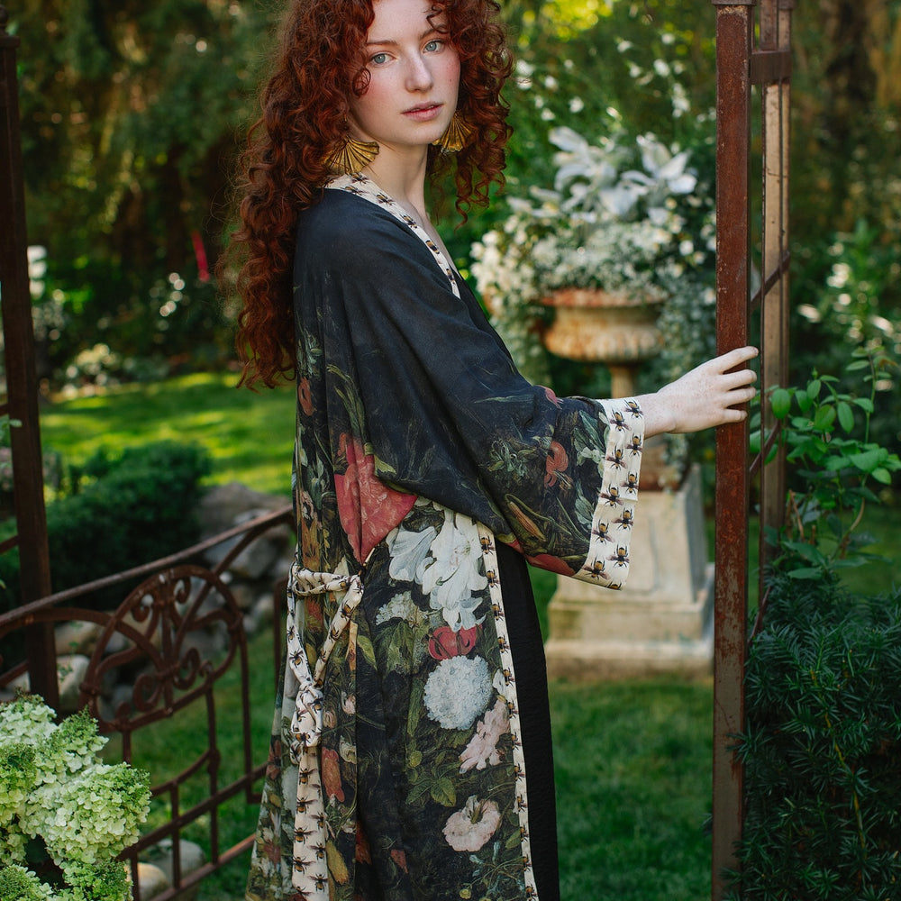 
                  
                    Model wearing the I Dream in Flowers Opera Duster featuring floral oil painting by Jan Brueghel and Victorian bumblebee trim – Market of Stars.
                  
                