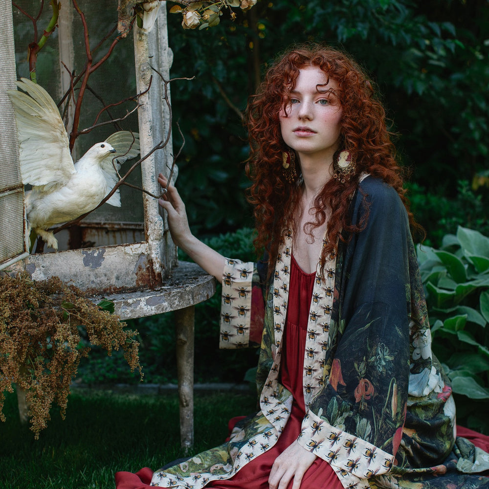 
                  
                    Model wearing the I Dream in Flowers Opera Duster featuring floral oil painting by Jan Brueghel and Victorian bumblebee trim – Market of Stars.
                  
                