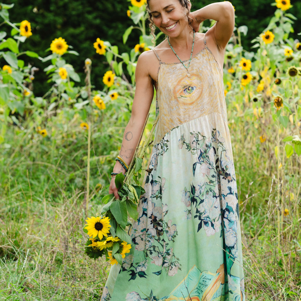 
                  
                    Model wearing bamboo viscose slip dress featuring Van Gogh artwork and quote, with painted blossoms, book, sun, and eye in rich sunny tones of jade and gold - Market of Stars
                  
                