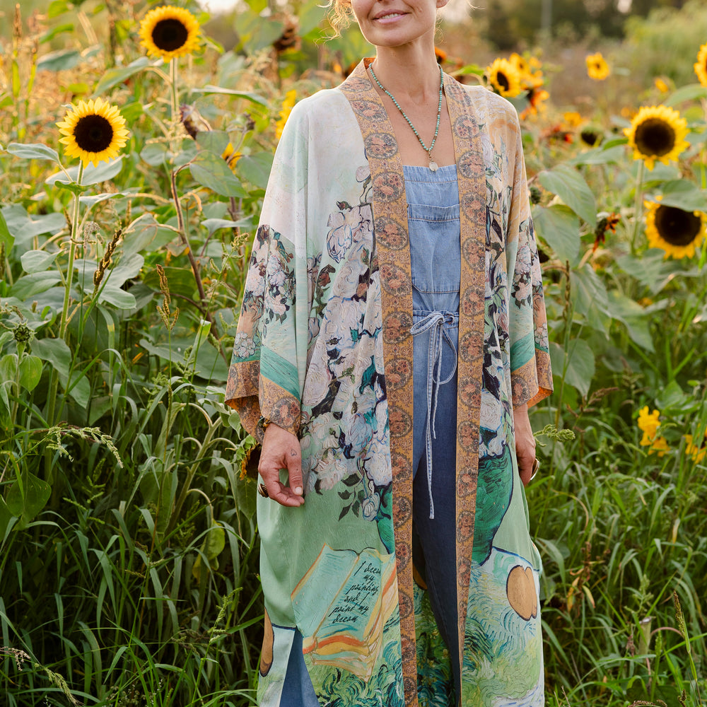 
                  
                    Model wearing long kimono duster featuring Van Gogh artwork and quote, with painted blossoms, book, sun, and eye in rich tones of jade and gold - Market of Stars
                  
                