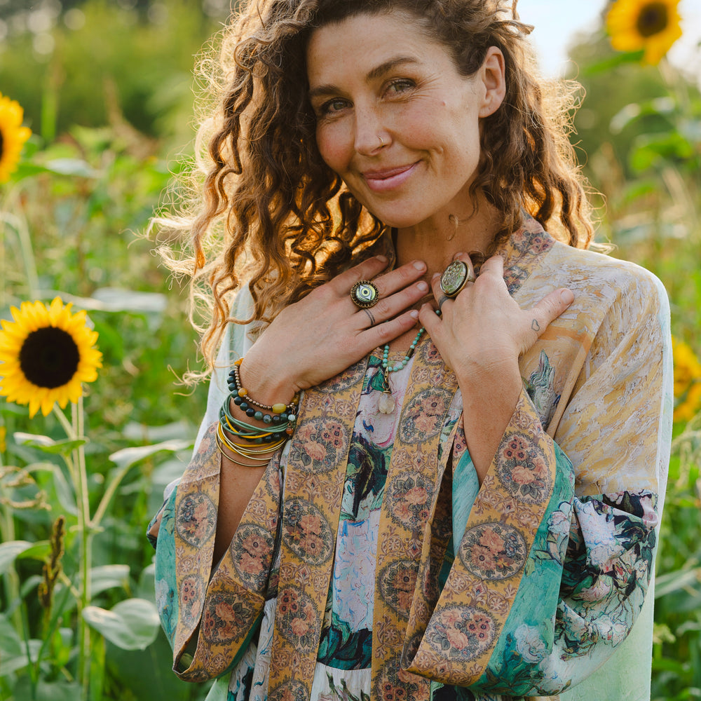
                  
                    Model wearing long kimono duster featuring Van Gogh artwork and quote, with painted blossoms, book, sun, and eye in rich tones of jade and gold - Market of Stars
                  
                