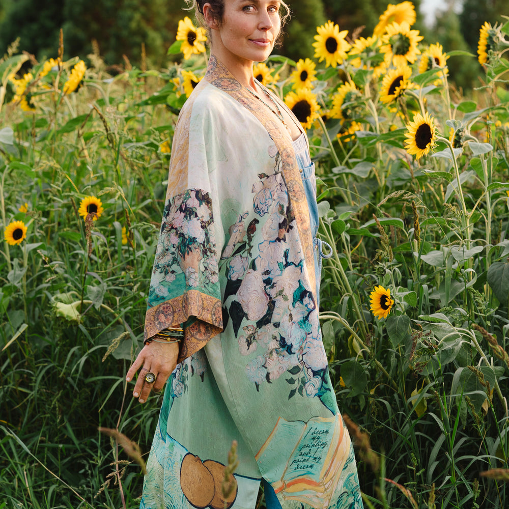 
                  
                    Model wearing long kimono duster featuring Van Gogh artwork and quote, with painted blossoms, book, sun, and eye in rich tones of jade and gold - Market of Stars
                  
                