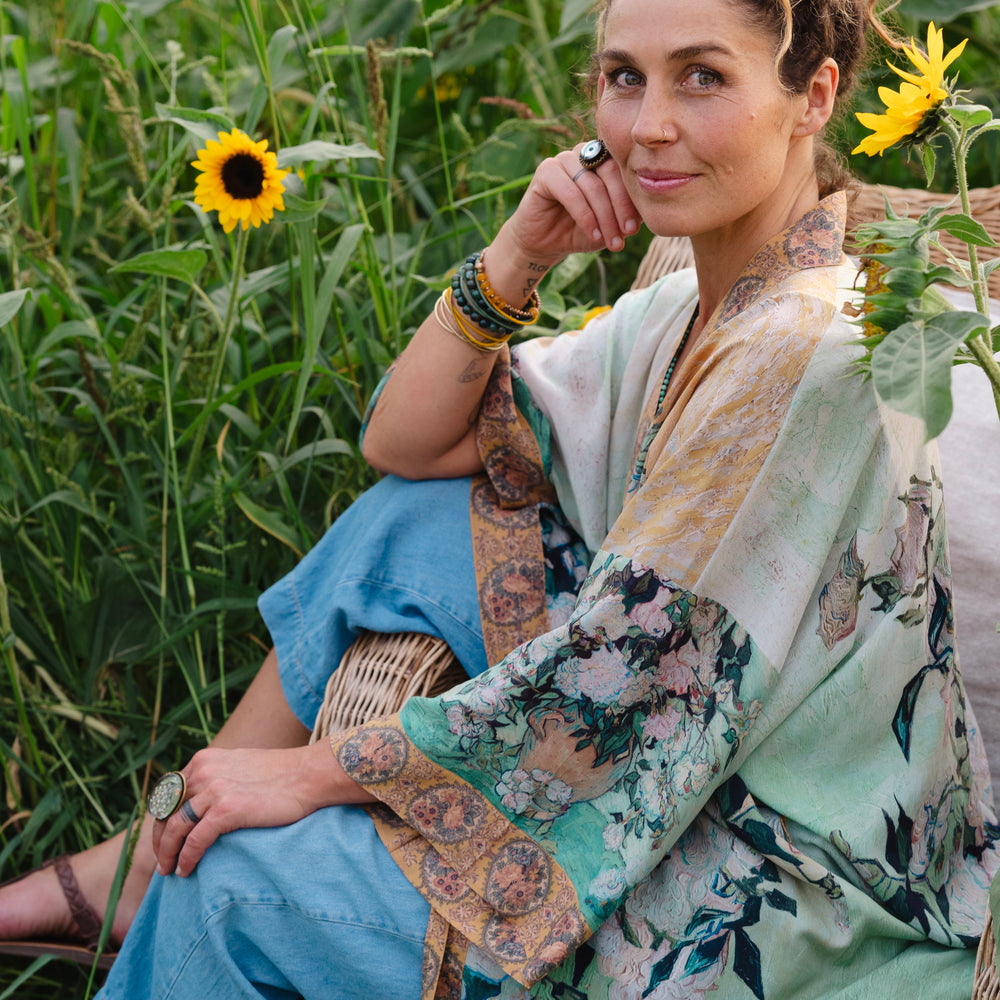 
                  
                    Model wearing long kimono duster featuring Van Gogh artwork and quote, with painted blossoms, book, sun, and eye in rich tones of jade and gold - Market of Stars
                  
                