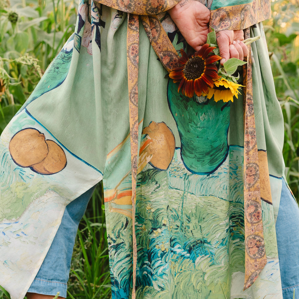 
                  
                    Model wearing long kimono duster featuring Van Gogh artwork and quote, with painted blossoms, book, sun, and eye in rich tones of jade and gold - Market of Stars
                  
                