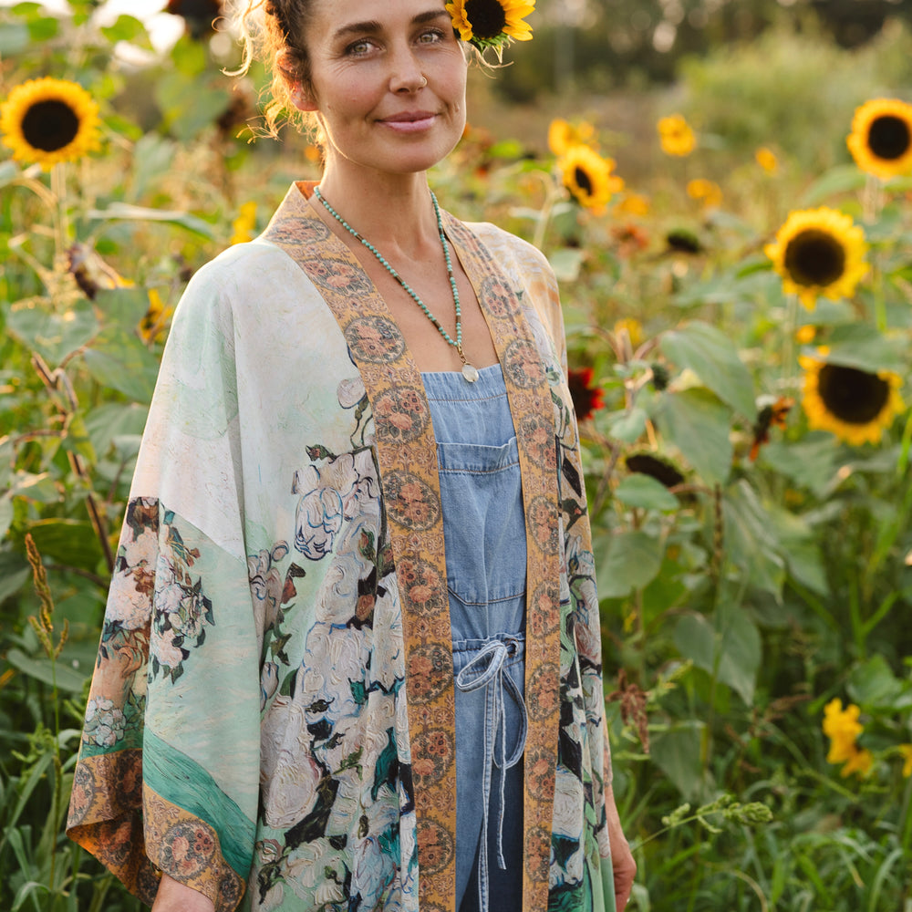 
                  
                    Model wearing long kimono duster featuring Van Gogh artwork and quote, with painted blossoms, book, sun, and eye in rich tones of jade and gold - Market of Stars
                  
                