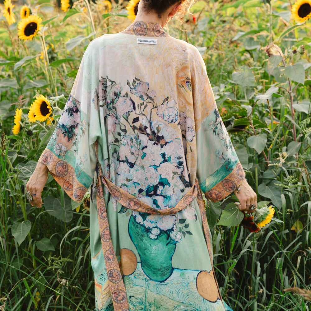 
                  
                    Model wearing long kimono duster featuring Van Gogh artwork and quote, with painted blossoms, book, sun, and eye in rich tones of jade and gold - Market of Stars
                  
                