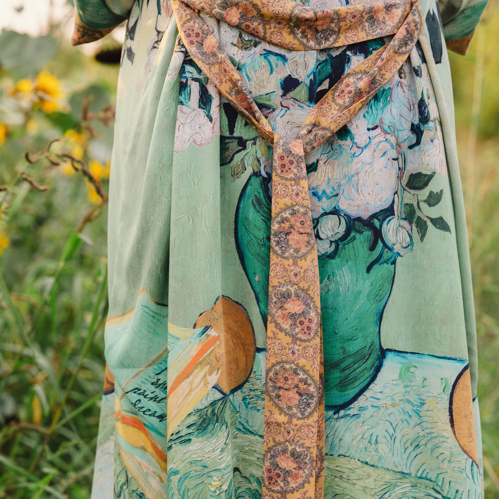 
                  
                    Model wearing long kimono duster featuring Van Gogh artwork and quote, with painted blossoms, book, sun, and eye in rich tones of jade and gold - Market of Stars
                  
                