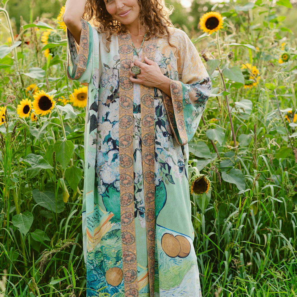 
                  
                    Model wearing long kimono duster featuring Van Gogh artwork and quote, with painted blossoms, book, sun, and eye in rich tones of jade and gold - Market of Stars
                  
                