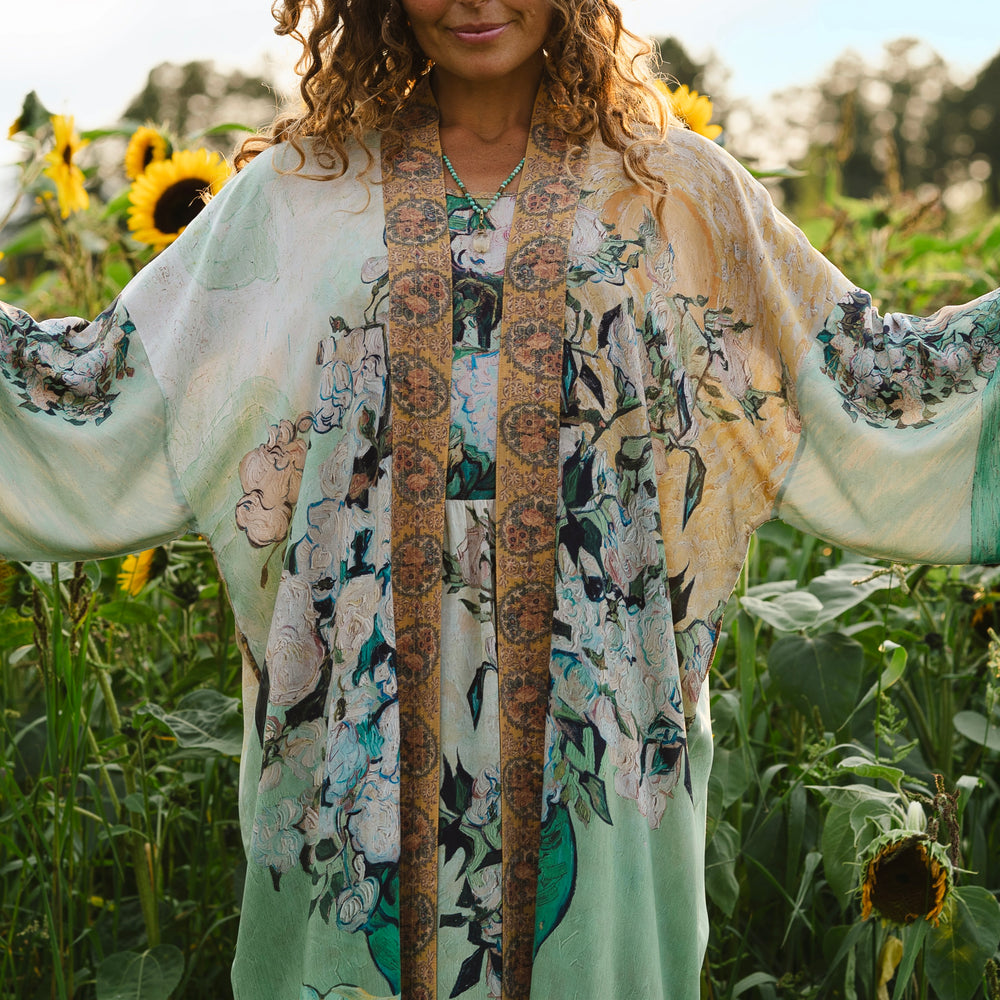 
                  
                    Model wearing long kimono duster featuring Van Gogh artwork and quote, with painted blossoms, book, sun, and eye in rich tones of jade and gold - Market of Stars
                  
                