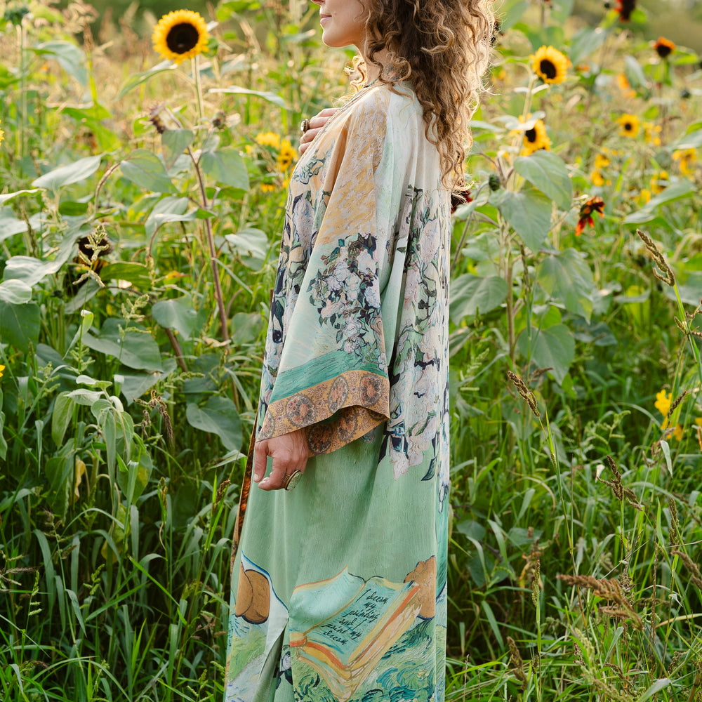 
                  
                    Model wearing long kimono duster featuring Van Gogh artwork and quote, with painted blossoms, book, sun, and eye in rich tones of jade and gold - Market of Stars
                  
                