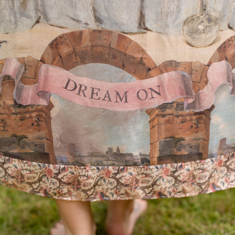 
                  
                    Model wearing the Imaginarium Bohéme Slip Dress featuring a dreamy layered print of historic landscapes, chandeliers, and a sleeping muse – Market of Stars.
                  
                