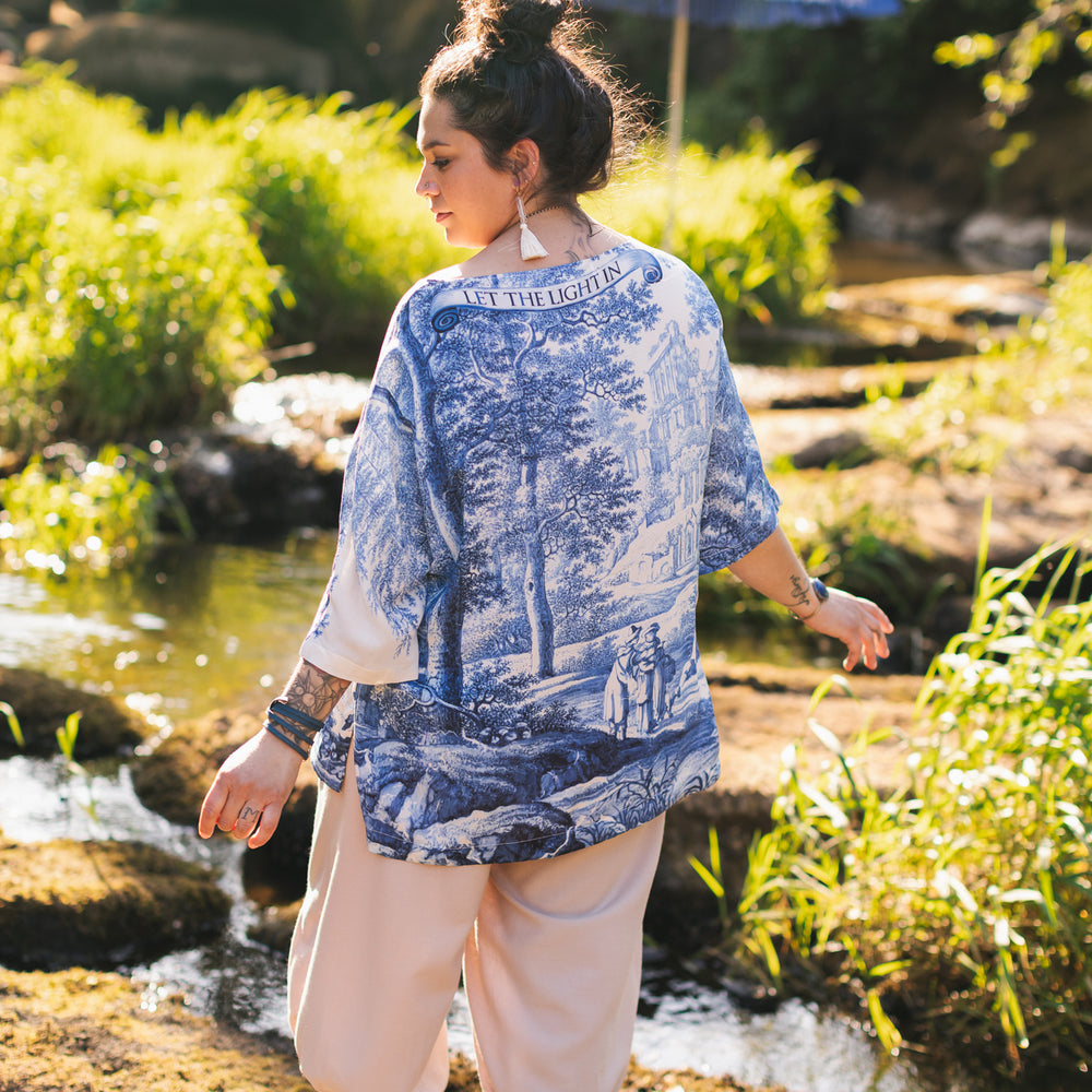 Model wearing Let the Light In bamboo viscose Luxe Tee shirt featuring print of Delft blue and white landscape pottery, and positive message of light and hope - Market of Stars
