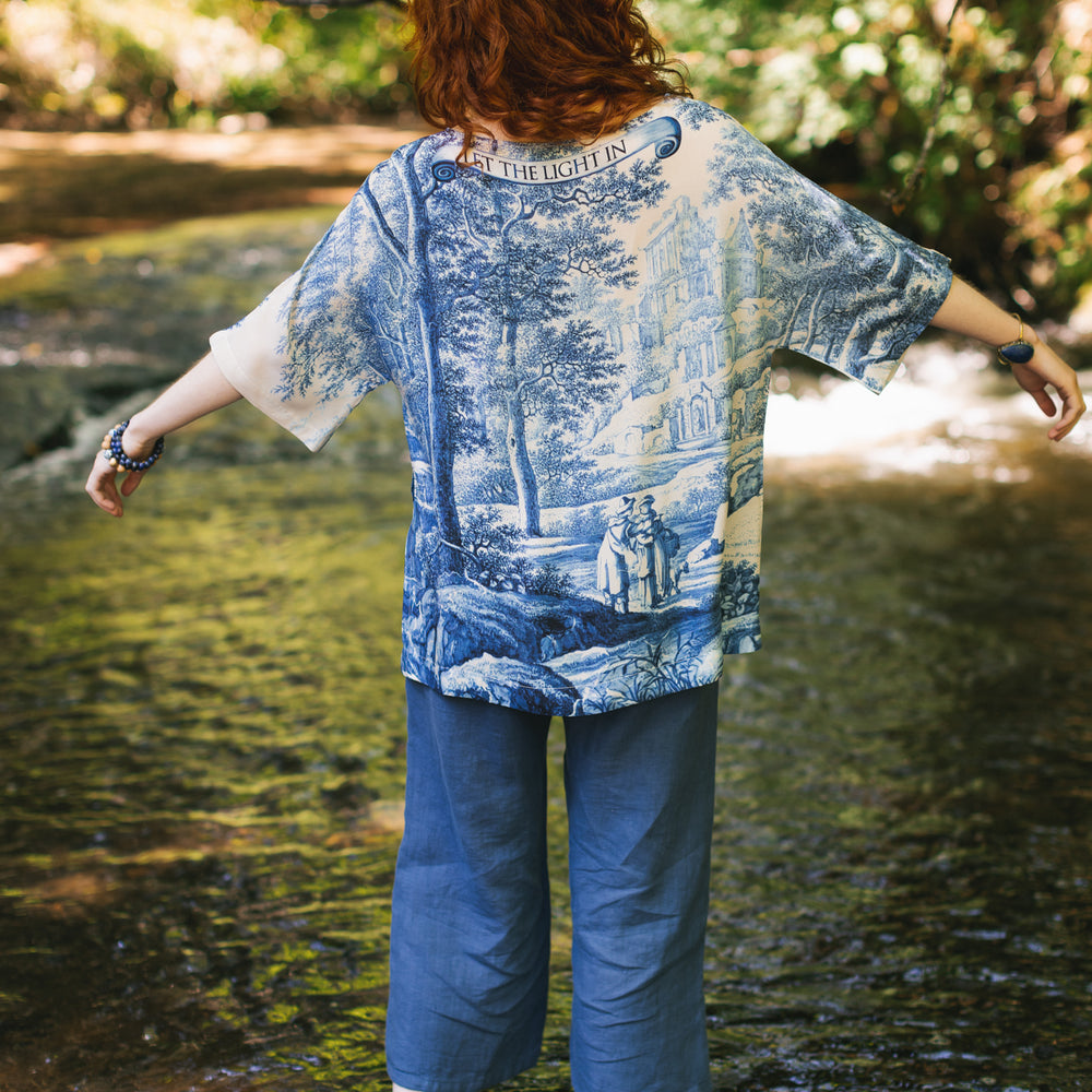 
                  
                    Model wearing Let the Light In bamboo viscose Luxe Tee shirt featuring print of Delft blue and white landscape pottery, and positive message of light and hope - Market of Stars
                  
                