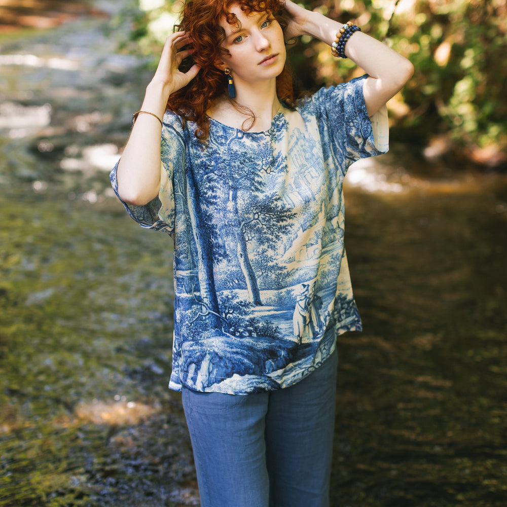 
                  
                    Model wearing Let the Light In bamboo viscose Luxe Tee shirt featuring print of Delft blue and white landscape pottery, and positive message of light and hope - Market of Stars
                  
                
