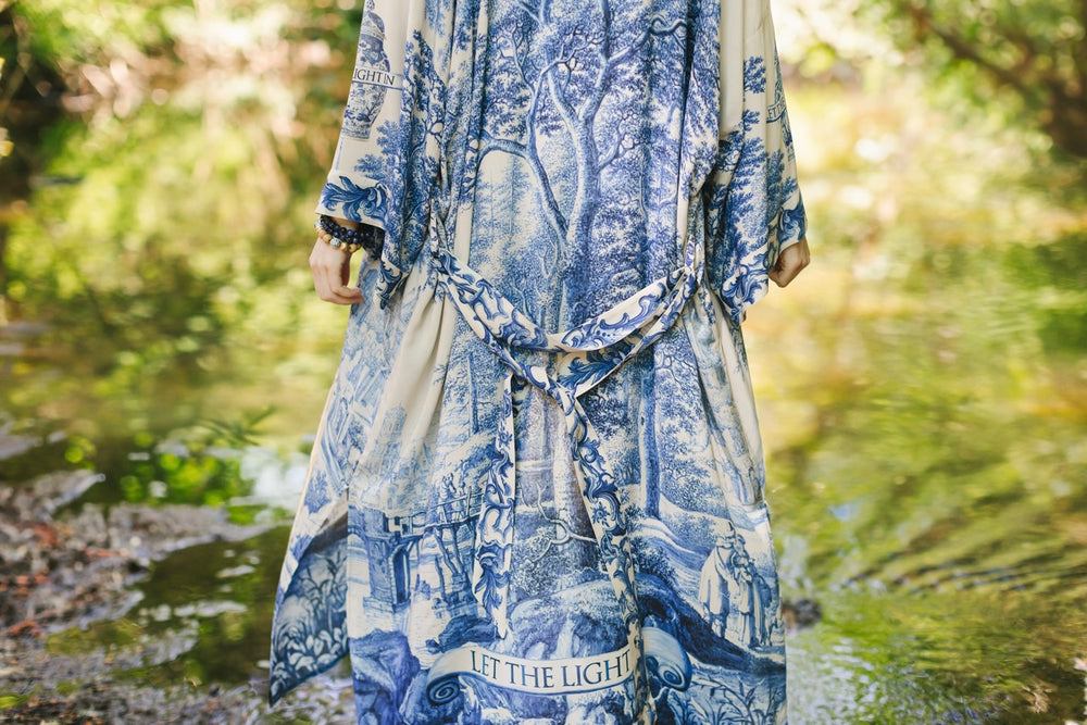 
                  
                    Model wearing Let the Light In long opera duster kimono featuring print of Delft blue and white landscape pottery, and positive message of light and hope - Market of Stars
                  
                
