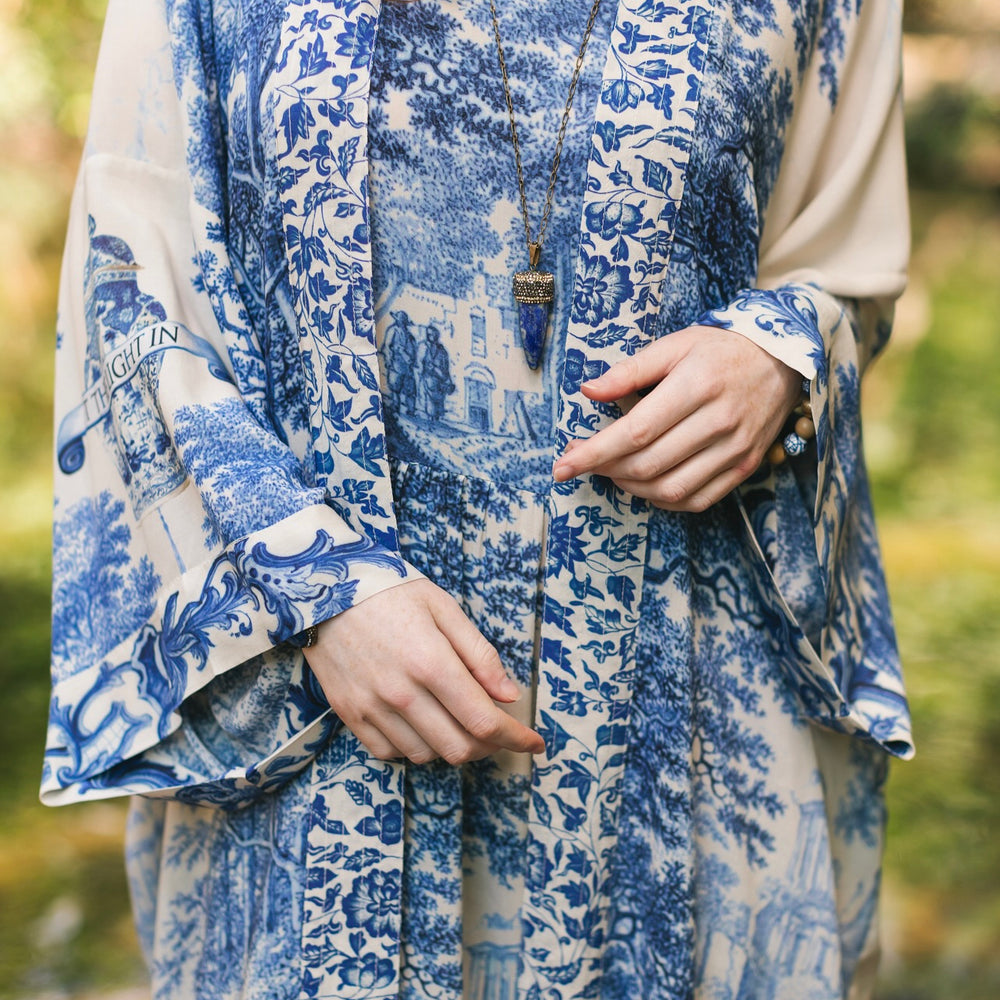 
                  
                    Model wearing Let the Light In long opera duster kimono featuring print of Delft blue and white landscape pottery, and positive message of light and hope - Market of Stars
                  
                