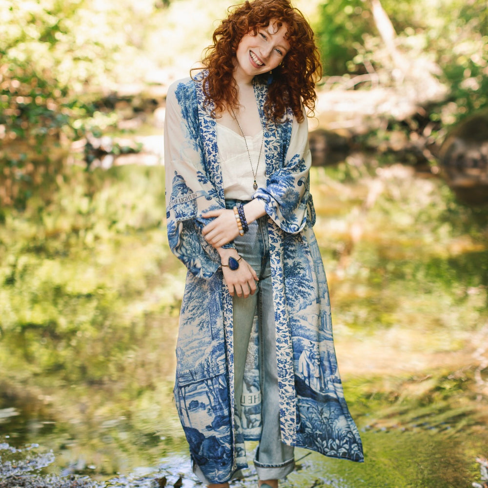 
                  
                    Model wearing Let the Light In long opera duster kimono featuring print of Delft blue and white landscape pottery, and positive message of light and hope - Market of Stars
                  
                