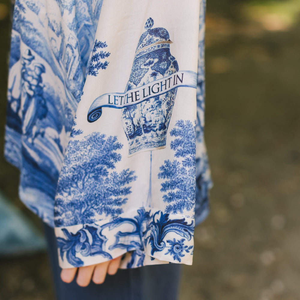 
                  
                    Model wearing Let the Light In cropped Pixie duster featuring print of Delft blue and white landscape pottery, and positive message of light and hope - Market of Stars
                  
                