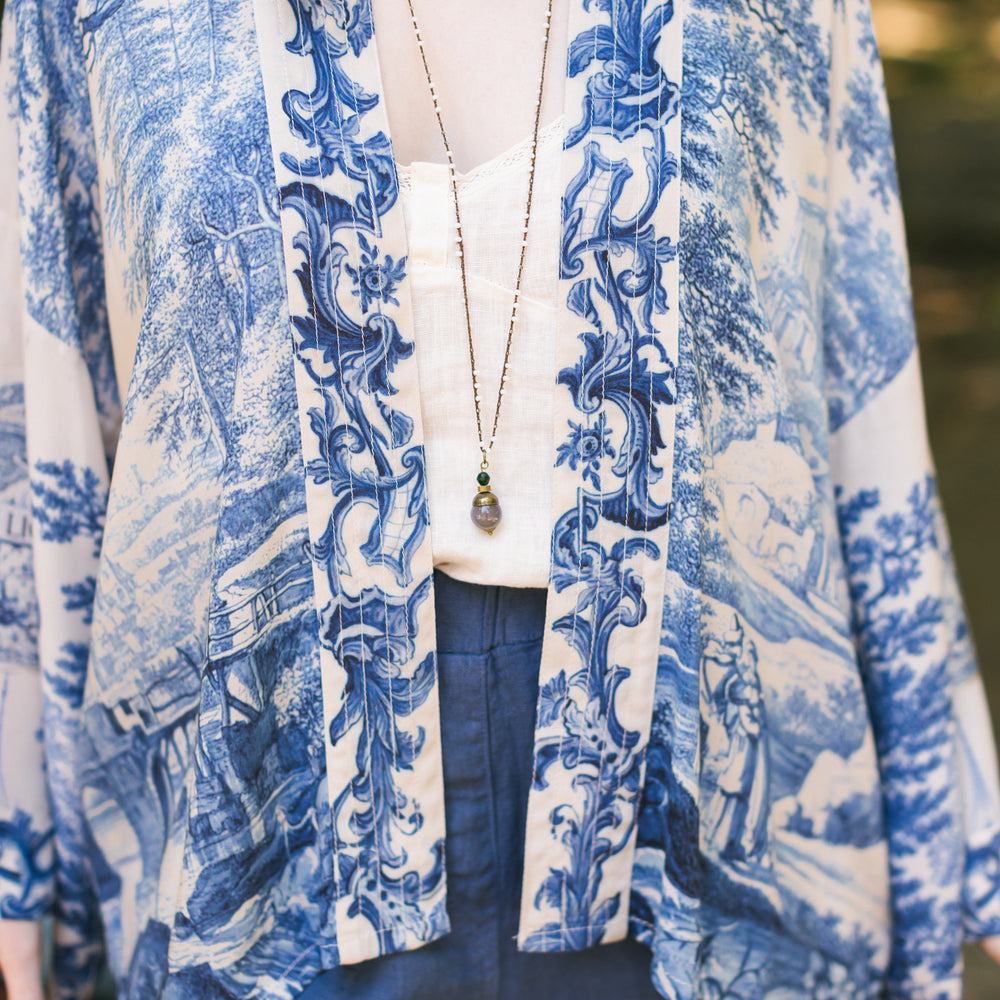 
                  
                    Model wearing Let the Light In cropped Pixie duster featuring print of Delft blue and white landscape pottery, and positive message of light and hope - Market of Stars
                  
                